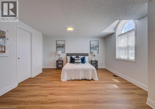 Spacious bedroom featuring wood-finish flooring, white baseboards, and a large arched window with blinds - 139 Werstine Terrace, Cambridge, ON 