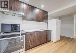 Kitchen featuring dark wood-finish cabinetry with silver hardware, light-toned countertops, a stainless steel range with overhead ventilation, and light wood-finish flooring - 