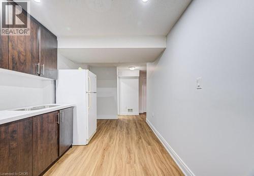 Kitchenette area featuring wood-finish cabinetry, a white countertop with an integrated stainless steel sink, and light wood-finish flooring - 139 Werstine Terrace, Cambridge, ON 