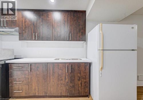 Kitchenette featuring wood-finish cabinetry with silver hardware, a white countertop, an integrated stainless steel sink, a white refrigerator, and recessed lighting - 139 Werstine Terrace, Cambridge, ON 
