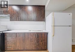 Kitchenette featuring wood-finish cabinetry with silver hardware, a white countertop, an integrated stainless steel sink, a white refrigerator, and recessed lighting - 