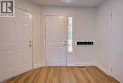 Entryway featuring wood-finish flooring, white paneled doors, and a vertical sidelight window - 