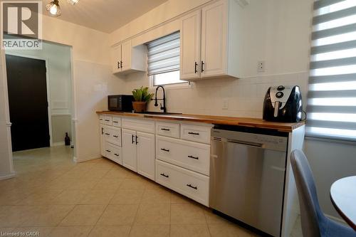 Kitchen featuring white cabinetry with matte black hardware, wood-finish countertops, stainless steel dishwasher, white subway tile backsplash, and a window with horizontal blinds - 147 Muriel Crescent, London, ON 