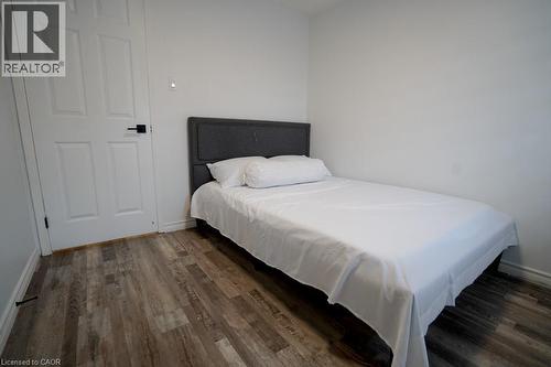 Bedroom featuring wood-finish flooring, a paneled door with black hardware, and white baseboards - 147 Muriel Crescent, London, ON 