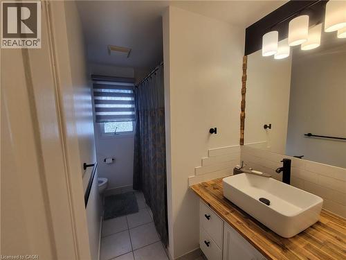 Modern bathroom featuring a rectangular vessel sink with a matte black faucet, set atop a wood-finish countertop - 147 Muriel Crescent, London, ON 