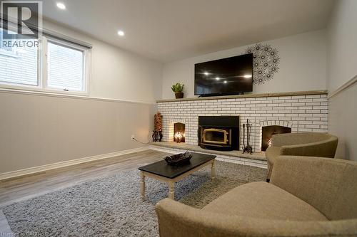 Built-in white brick fireplace with a wood-burning insert and two additional hearths, recessed lighting, wood-finish flooring, and a large window - 147 Muriel Crescent, London, ON 