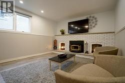 Built-in white brick fireplace with a wood-burning insert and two additional hearths, recessed lighting, wood-finish flooring, and a large window - 