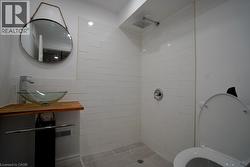 Bathroom featuring a vessel sink with a wood-finish countertop, a wall-mounted faucet, and a circular mirror - 