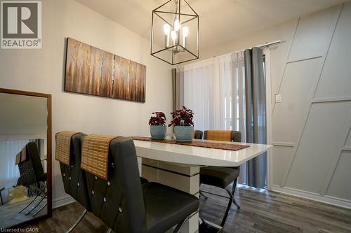 Dining area featuring wood-finish flooring, a contemporary geometric accent wall, and a sliding glass door with sheer and solid panel curtains - 147 Muriel Crescent, London, ON 