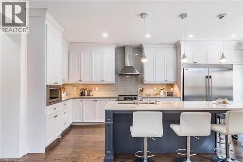 Kitchen featuring white shaker-style cabinetry, a contrasting island with a quartz countertop, stainless steel appliances, a tiled backsplash, and recessed lighting - 47 Hawke Crescent, New Tecumseth, ON 