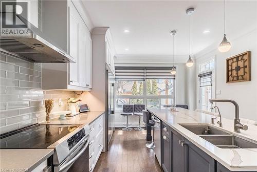 Gourmet kitchen featuring a stainless steel range hood, white shaker-style cabinetry, subway tile backsplash, a built-in electric range, and a large central island with a double basin sink and pendant - 47 Hawke Crescent, New Tecumseth, ON 