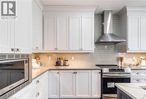 Contemporary kitchen featuring white cabinetry with brushed nickel hardware, light gray subway tile backsplash, stainless steel range hood, built-in microwave, and stone countertops - 47 Hawke Crescent, New Tecumseth, ON 