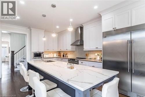 Modern kitchen featuring a large central island with a quartz countertop, white shaker-style cabinetry, stainless steel appliances, and wood-finish flooring - 47 Hawke Crescent, New Tecumseth, ON 