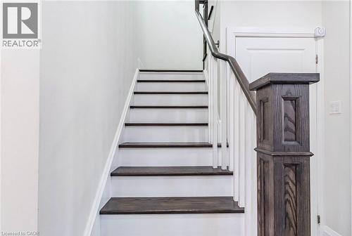 Staircase featuring dark wood-finish treads, white risers, and a prominent wood-finish newel post with a matching handrail - 47 Hawke Crescent, New Tecumseth, ON 