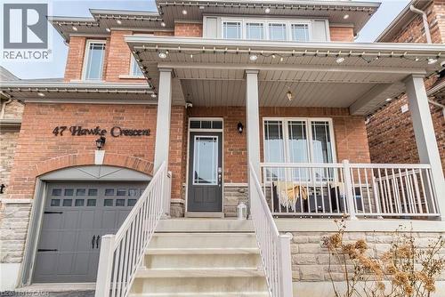 Brick facade residence featuring a covered front porch with white railings, a single-car garage with an arched brick header, and stone detailing along the lower exterior - 47 Hawke Crescent, New Tecumseth, ON 