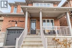Brick facade residence featuring a covered front porch with white railings, a single-car garage with an arched brick header, and stone detailing along the lower exterior - 