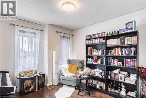 Room featuring two large windows with white sheers, dark wood-finish flooring, a contemporary ceiling light fixture, and extensive built-in shelving - 47 Hawke Crescent, New Tecumseth, ON 