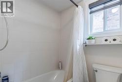 White tiled shower-tub combination featuring a window with a roller shade - 