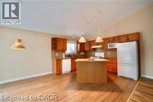 Vaulted ceilings accent this kitchen featuring wood-finish flooring, wood cabinetry, a central island, and white appliances - 17 Hawkswood Drive, Kitchener, ON 