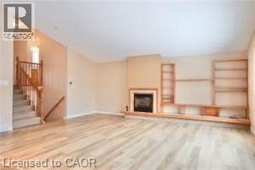 Spacious living area featuring light wood-finish flooring, a central fireplace with a mantel, and extensive built-in shelving - 17 Hawkswood Drive, Kitchener, ON 