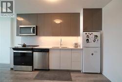 Contemporary kitchen featuring two-tone cabinetry, stainless steel appliances, a built-in microwave, and wood-finish flooring - 