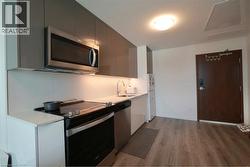 Modern kitchen featuring sleek gray cabinetry, stainless steel microwave, integrated cooktop, undermount sink, and light wood-finish flooring - 