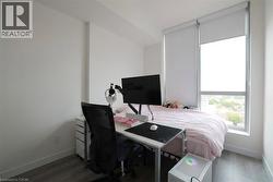 Bedroom featuring a large window with roller shades, light grey wood-finish flooring, and white painted walls - 