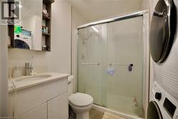 Bathroom featuring a single vanity with an integrated sink, a mirrored medicine cabinet, a sliding glass door shower, and a stacked washer and dryer unit - 