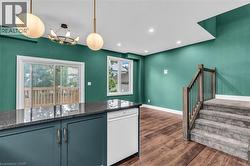 Open-concept interior featuring wood-finish flooring, recessed lighting, and a modern kitchen island with dark cabinetry and a stone countertop - 
