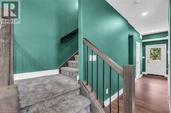 Entryway featuring a wood-finish flooring, a contemporary staircase with wood-finish handrails and black metal balusters, green accent walls, and recessed lighting - 