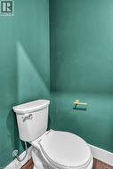 White toilet with a chrome flush lever, set against teal walls with white baseboards, and wood-finish flooring - 