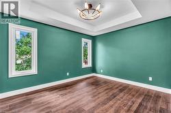 Spacious room featuring wood-finish flooring, a tray ceiling with a modern light fixture, and two windows providing natural illumination - 