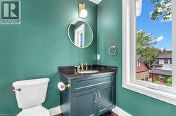 Powder room featuring a single-pane window, a dark teal vanity with golden hardware, a granite countertop, and wood-finish flooring - 