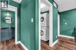 Hallway featuring wood-finish flooring, a stacked washer and dryer, and a built-in vanity with a dark countertop and gold-finish fixtures - 