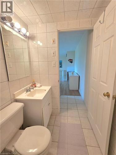 Bathroom featuring floor-to-ceiling white tile, a white vanity with integrated sink, a mirrored wall cabinet, and a chrome light fixture - 2373 E King Street E Unit# 37, Hamilton, ON 