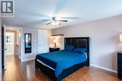 Bedroom featuring wood-finish flooring, a ceiling fan with integrated lighting, and a white interior door - 