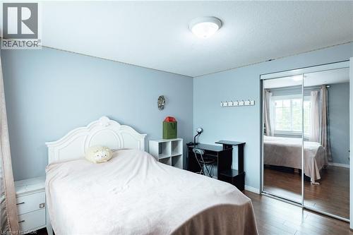 Bedroom featuring wood-finish flooring, light blue walls, a window with natural light, and a built-in mirrored closet - 171 Mcnichol Drive, Cambridge, ON 
