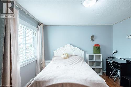 Bedroom featuring wood-finish flooring, a window with blinds, a white decorative headboard, and a flush-mount ceiling light fixture - 171 Mcnichol Drive, Cambridge, ON 