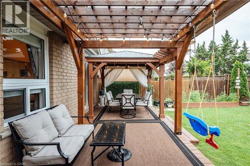 Expansive backyard featuring a wood pergola with string lighting, a dedicated gazebo dining area with privacy drapes, a brick exterior, a wood-planked patio, and a manicured lawn - 171 Mcnichol Drive, Cambridge, ON 