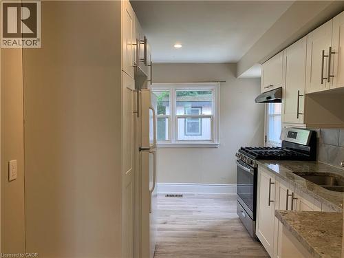 Unit 2 updated kitchen featuring light-colored cabinetry, stainless steel range and hood, dual basin sink, and granite-look countertops - 405 Macnab Street N, Hamilton, ON 