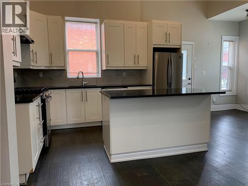 Unit 1 kitchen featuring white shaker cabinetry, dark countertops, stainless steel appliances, a center island, and wood-finish flooring - 405 Macnab Street N, Hamilton, ON 