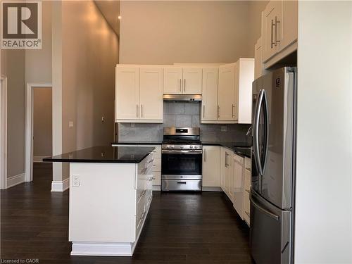 Unit 1Modern kitchen featuring an extended island with a black countertop, white shaker-style cabinetry, stainless steel appliances, and dark wood-finish flooring - 405 Macnab Street N, Hamilton, ON 