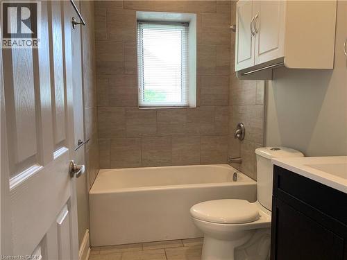 Unit 1 Bathroom featuring a white bathtub, ceramic tile surround, window with blinds, and white toilet - 405 Macnab Street N, Hamilton, ON 