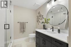 Bathroom featuring a dark wood-finish vanity with a white countertop and undermount sink, a circular framed mirror, and a glass-enclosed shower - 
