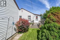 Rear exterior, featuring a wooden deck with steps, a manicured lawn, and mature landscaping - 