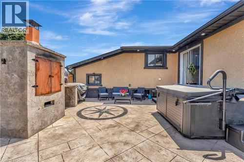 Stamped concrete patio featuring an outdoor cooking structure with a chimney, a built-in hot tub, a compass rose inlay, and a sliding glass door entry to the building - 192 Myers Road, Cambridge, ON 