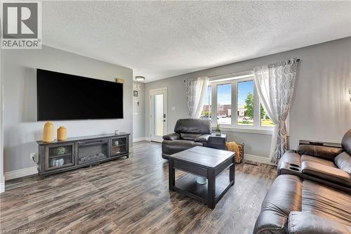 Spacious living area featuring wood-finish flooring, light gray walls, a large multi-pane window, and a built-in media console with glass-front cabinets - 192 Myers Road, Cambridge, ON 