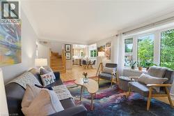 Expansive living area with wood-finish flooring, a bright bay window, and a visible staircase - 