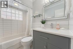 Full bathroom featuring a single vanity with a white countertop and gray cabinetry, a framed mirror, a tub/shower combination with white subway tile surround, and a glass block window - 
