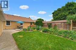 Expansive backyard featuring a manicured lawn, concrete patio, and garden beds with established plantings - 